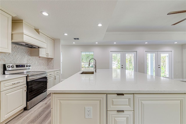 kitchen with premium range hood, french doors, an island with sink, and stainless steel electric range