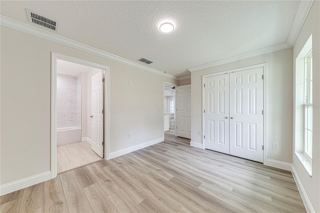 unfurnished bedroom with light wood-type flooring, a textured ceiling, connected bathroom, multiple windows, and a closet