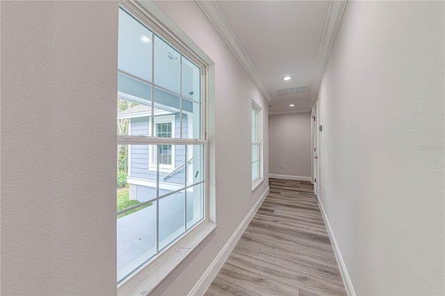 corridor with light wood-type flooring, crown molding, and a wealth of natural light