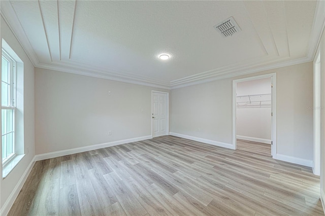 empty room with crown molding, a textured ceiling, and light wood-type flooring