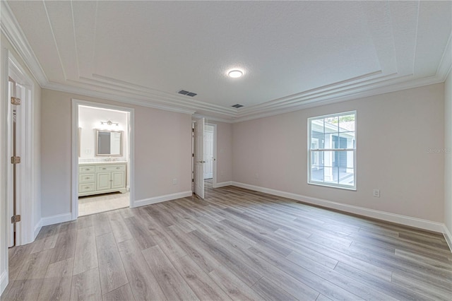 empty room featuring a tray ceiling, crown molding, a textured ceiling, and light wood-type flooring