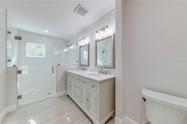 bathroom with a textured ceiling, vanity, an enclosed shower, and toilet