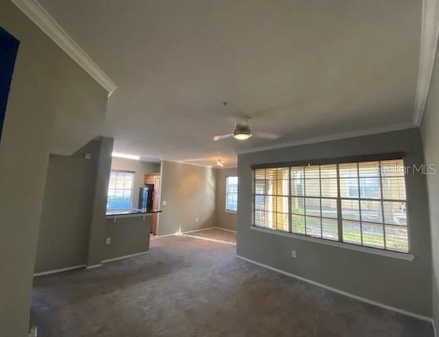 spare room featuring ceiling fan, dark carpet, crown molding, and a wealth of natural light