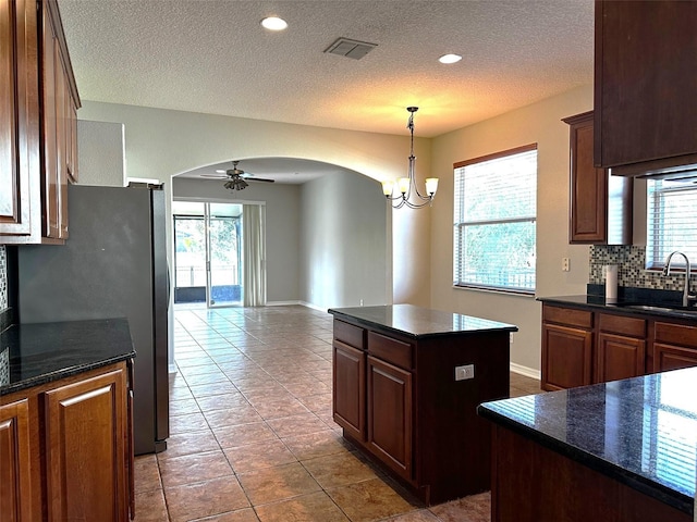 kitchen featuring dark tile patterned flooring, ceiling fan with notable chandelier, sink, stainless steel fridge, and a kitchen island