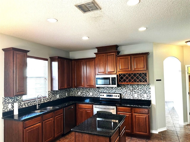 kitchen featuring a center island, dark stone counters, sink, dark tile patterned floors, and appliances with stainless steel finishes