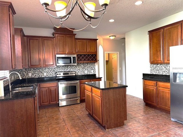 kitchen featuring a textured ceiling, stainless steel appliances, sink, a notable chandelier, and a kitchen island