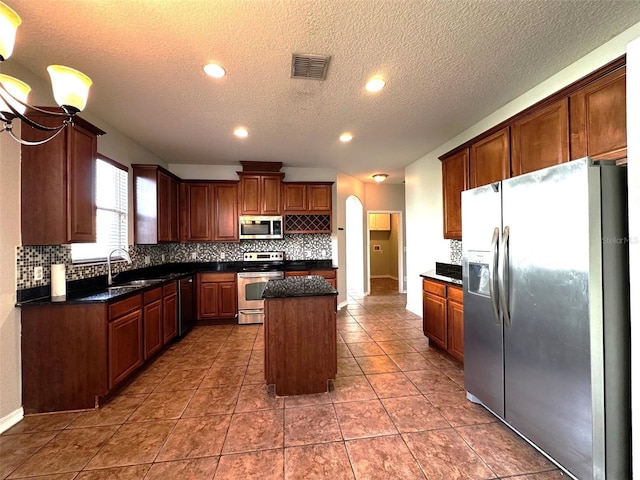 kitchen with a center island, dark tile patterned flooring, sink, a textured ceiling, and stainless steel appliances