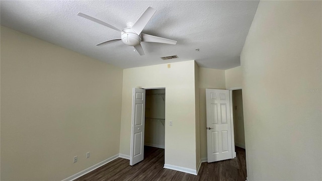 unfurnished bedroom featuring a walk in closet, a textured ceiling, ceiling fan, dark hardwood / wood-style floors, and a closet