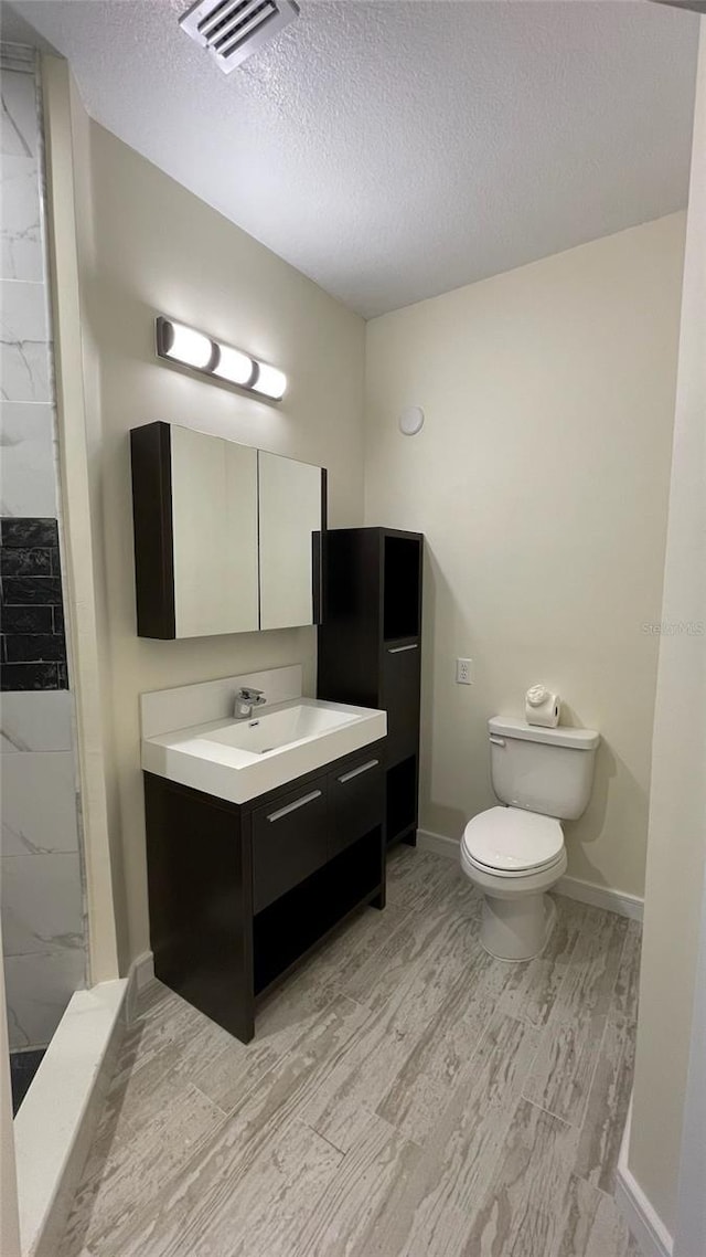 bathroom with a shower, wood-type flooring, a textured ceiling, toilet, and vanity