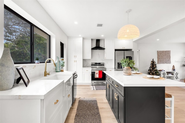 kitchen with stainless steel appliances, wall chimney range hood, white cabinets, a kitchen island, and hanging light fixtures