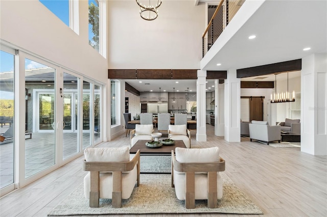 living room featuring a high ceiling, a chandelier, a barn door, and light wood-type flooring