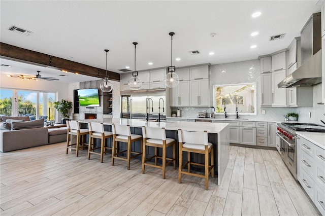 kitchen featuring a spacious island, beam ceiling, a breakfast bar area, double oven range, and wall chimney exhaust hood