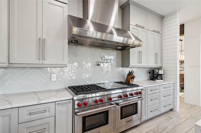 kitchen with light hardwood / wood-style flooring, wall chimney exhaust hood, tasteful backsplash, light stone countertops, and range with two ovens