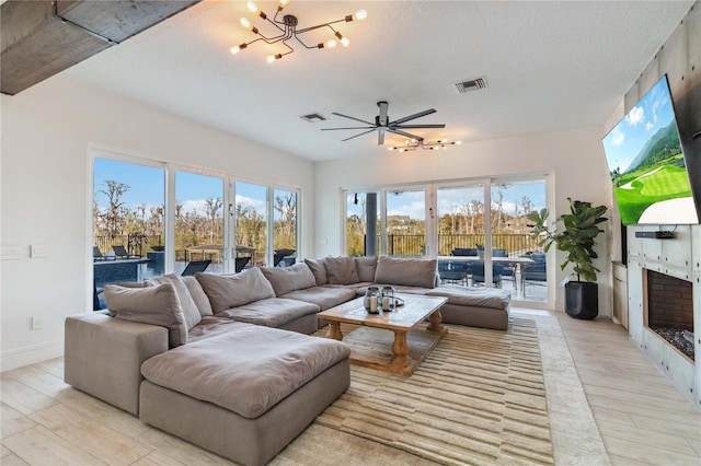 living room featuring a fireplace, a textured ceiling, light hardwood / wood-style floors, and ceiling fan with notable chandelier