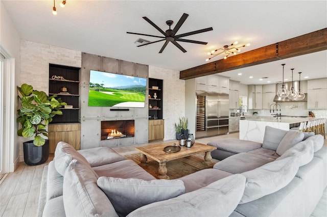 living room featuring ceiling fan, light wood-type flooring, beam ceiling, and a fireplace