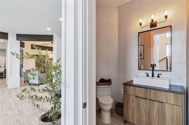 bathroom with hardwood / wood-style flooring, toilet, tile walls, and vanity