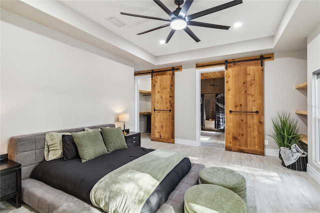 bedroom featuring a walk in closet, a closet, ceiling fan, light hardwood / wood-style flooring, and a barn door