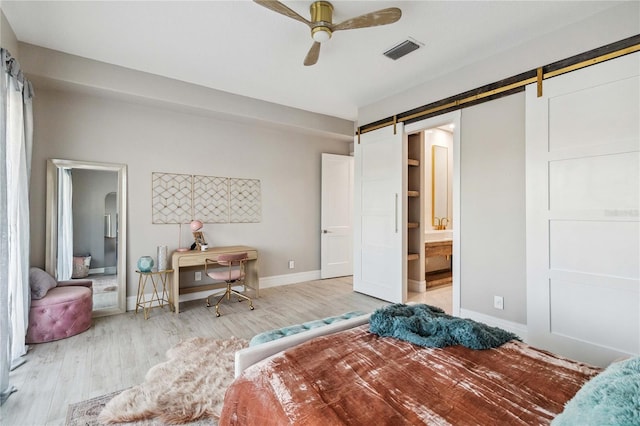 bedroom featuring light hardwood / wood-style flooring, connected bathroom, ceiling fan, and a barn door