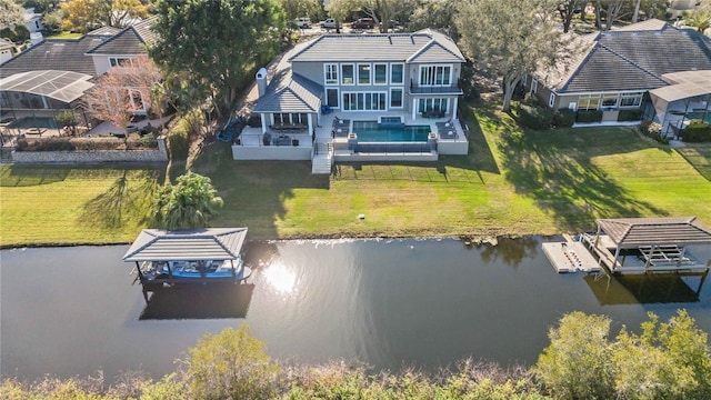 rear view of house with a water view, a lawn, and a jacuzzi