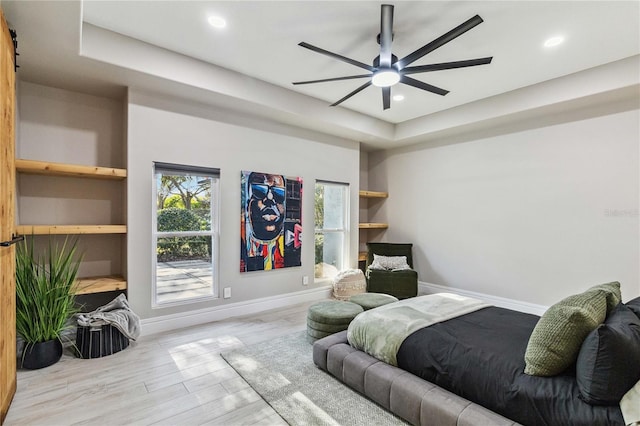 bedroom with light wood-type flooring, ceiling fan, and a tray ceiling