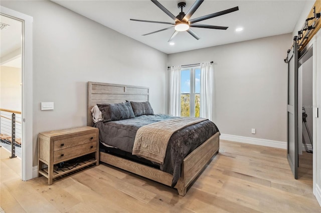 bedroom featuring ceiling fan, a barn door, and light hardwood / wood-style floors