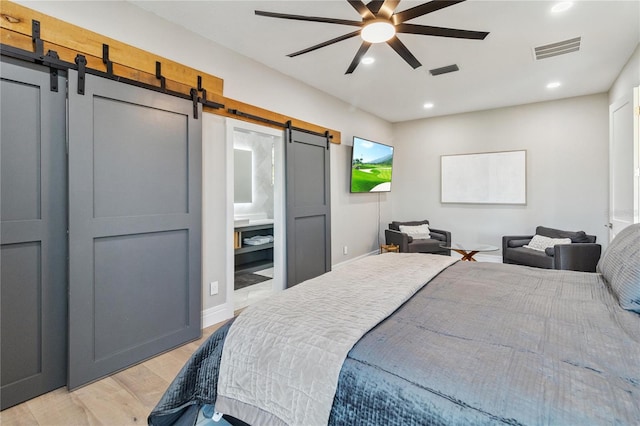 bedroom with ensuite bath, light hardwood / wood-style flooring, ceiling fan, and a barn door