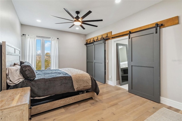 bedroom featuring light wood-type flooring, ceiling fan, and a barn door