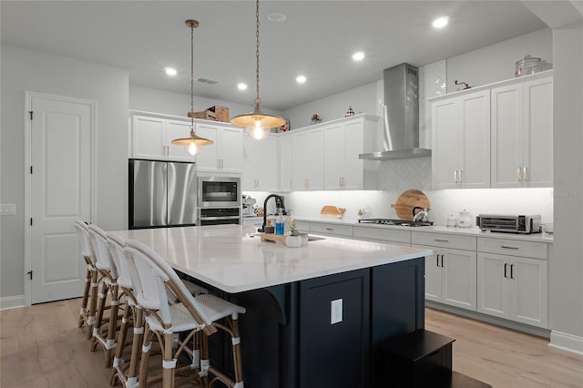 kitchen featuring white cabinetry, wall chimney range hood, sink, and appliances with stainless steel finishes