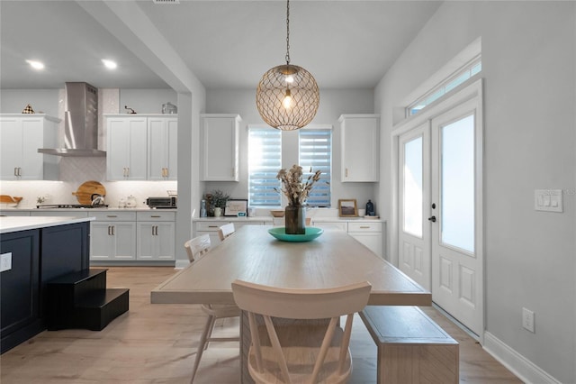 kitchen with pendant lighting, backsplash, wall chimney range hood, a kitchen island, and white cabinetry