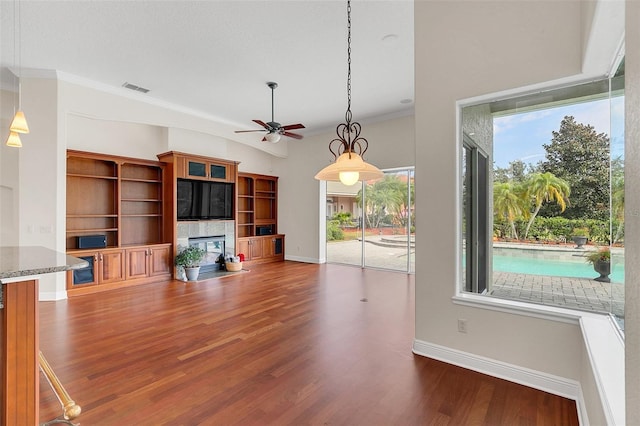 unfurnished living room with ceiling fan, wood-type flooring, ornamental molding, and a tiled fireplace