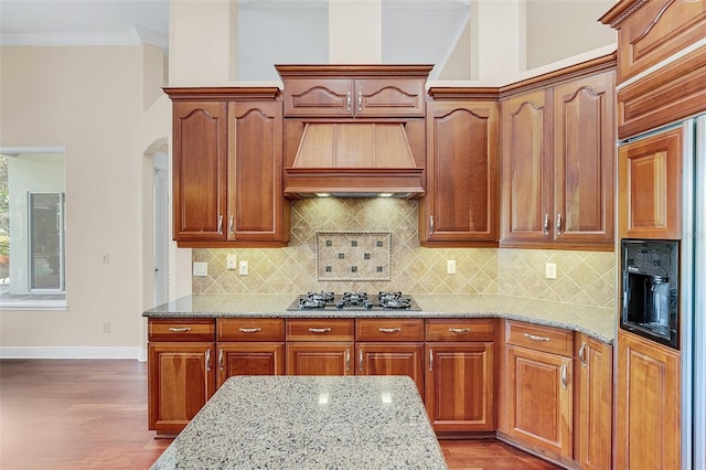 kitchen featuring black gas cooktop, paneled built in refrigerator, light stone countertops, tasteful backsplash, and custom range hood