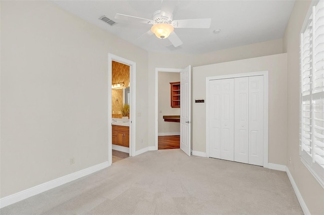 unfurnished bedroom featuring connected bathroom, ceiling fan, a closet, and light colored carpet