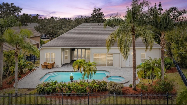 back house at dusk featuring a patio and a pool with hot tub