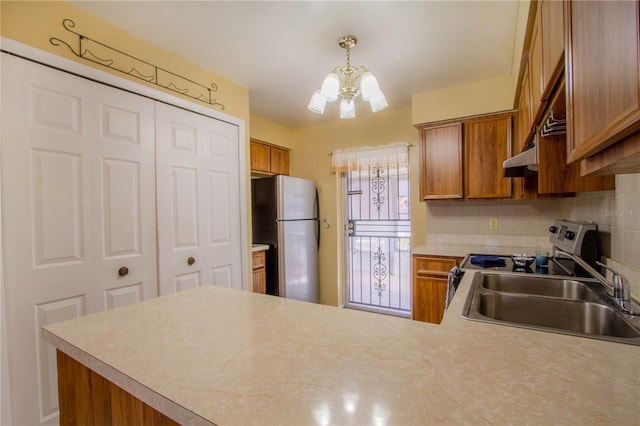 kitchen with kitchen peninsula, appliances with stainless steel finishes, sink, a notable chandelier, and hanging light fixtures