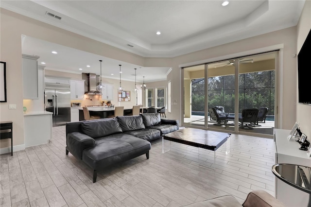 living room with a raised ceiling, ceiling fan, and ornamental molding