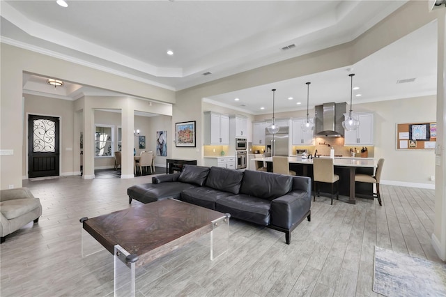 living room featuring light hardwood / wood-style floors, a raised ceiling, and ornamental molding