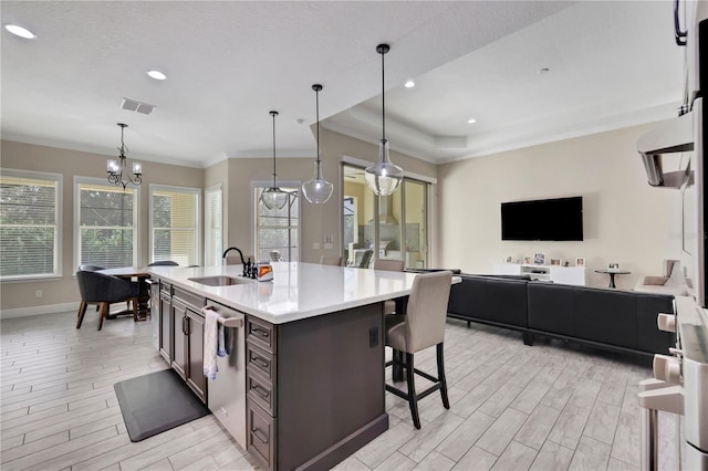 kitchen featuring sink, an inviting chandelier, stainless steel dishwasher, decorative light fixtures, and a center island with sink