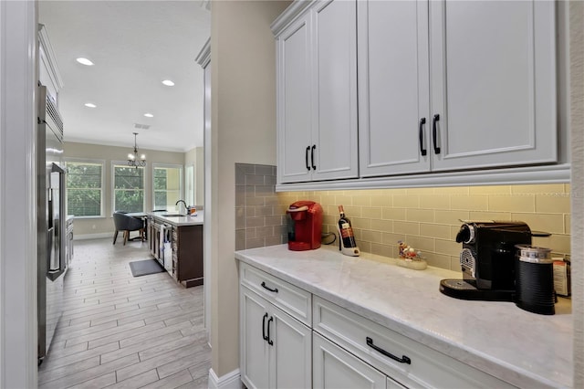 kitchen with white cabinetry, light stone countertops, sink, a chandelier, and high end fridge