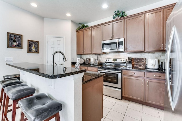 kitchen with appliances with stainless steel finishes, light tile patterned floors, a breakfast bar area, and an island with sink