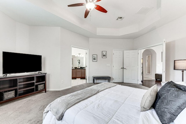 carpeted bedroom featuring a tray ceiling, ceiling fan, and ensuite bathroom