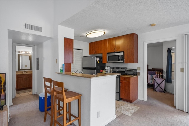 kitchen featuring light carpet, a textured ceiling, appliances with stainless steel finishes, a kitchen bar, and kitchen peninsula