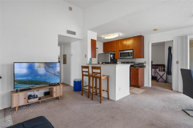 kitchen with a kitchen bar, a textured ceiling, light colored carpet, kitchen peninsula, and stainless steel appliances