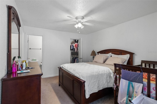 bedroom featuring light carpet, a textured ceiling, ceiling fan, a spacious closet, and a closet