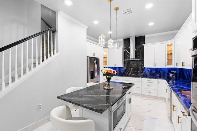 kitchen featuring backsplash, wall chimney range hood, appliances with stainless steel finishes, a kitchen island, and white cabinetry