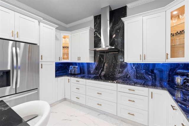 kitchen with wall chimney exhaust hood, stainless steel fridge, dark stone counters, decorative backsplash, and white cabinets