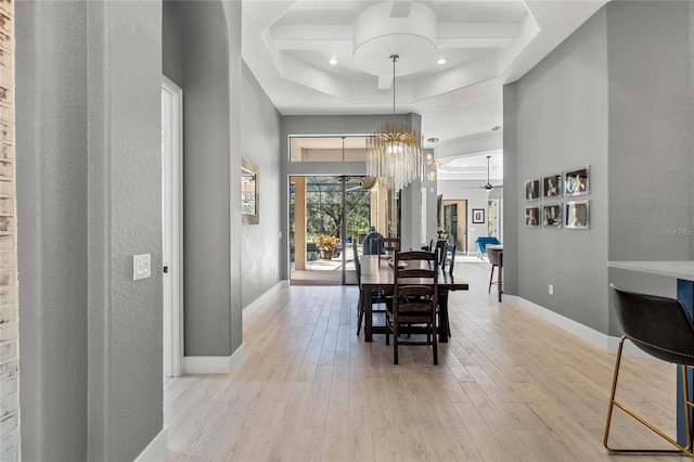 dining area with coffered ceiling, light hardwood / wood-style flooring, ceiling fan with notable chandelier, and a high ceiling