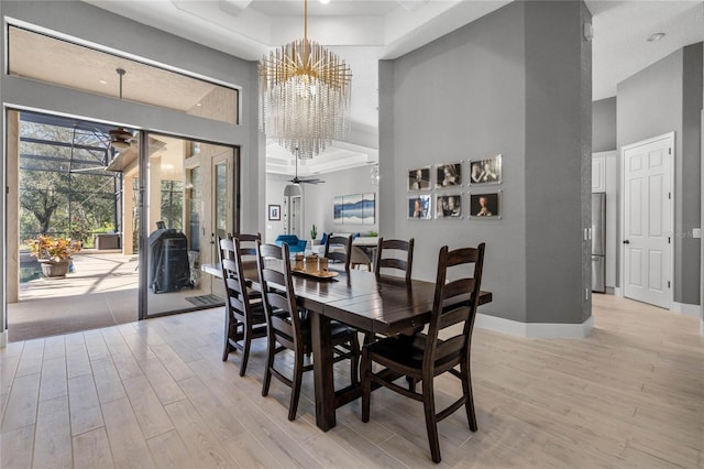 dining room with a high ceiling, ceiling fan with notable chandelier, and light hardwood / wood-style floors