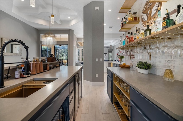 kitchen with ceiling fan with notable chandelier, sink, blue cabinetry, light hardwood / wood-style flooring, and hanging light fixtures