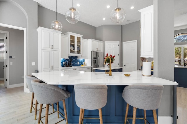 kitchen with white cabinets, decorative light fixtures, stainless steel fridge, and backsplash