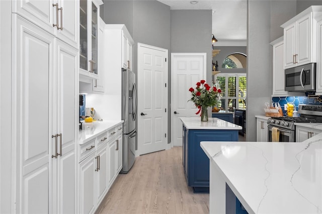 kitchen featuring a center island, white cabinets, light stone countertops, blue cabinetry, and stainless steel appliances